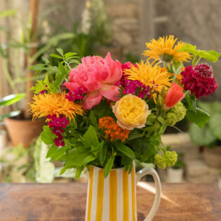 Bouquet de fleurs colorées orange et fuchsia dans un vase rayé – Parenthèse Florale Lyon