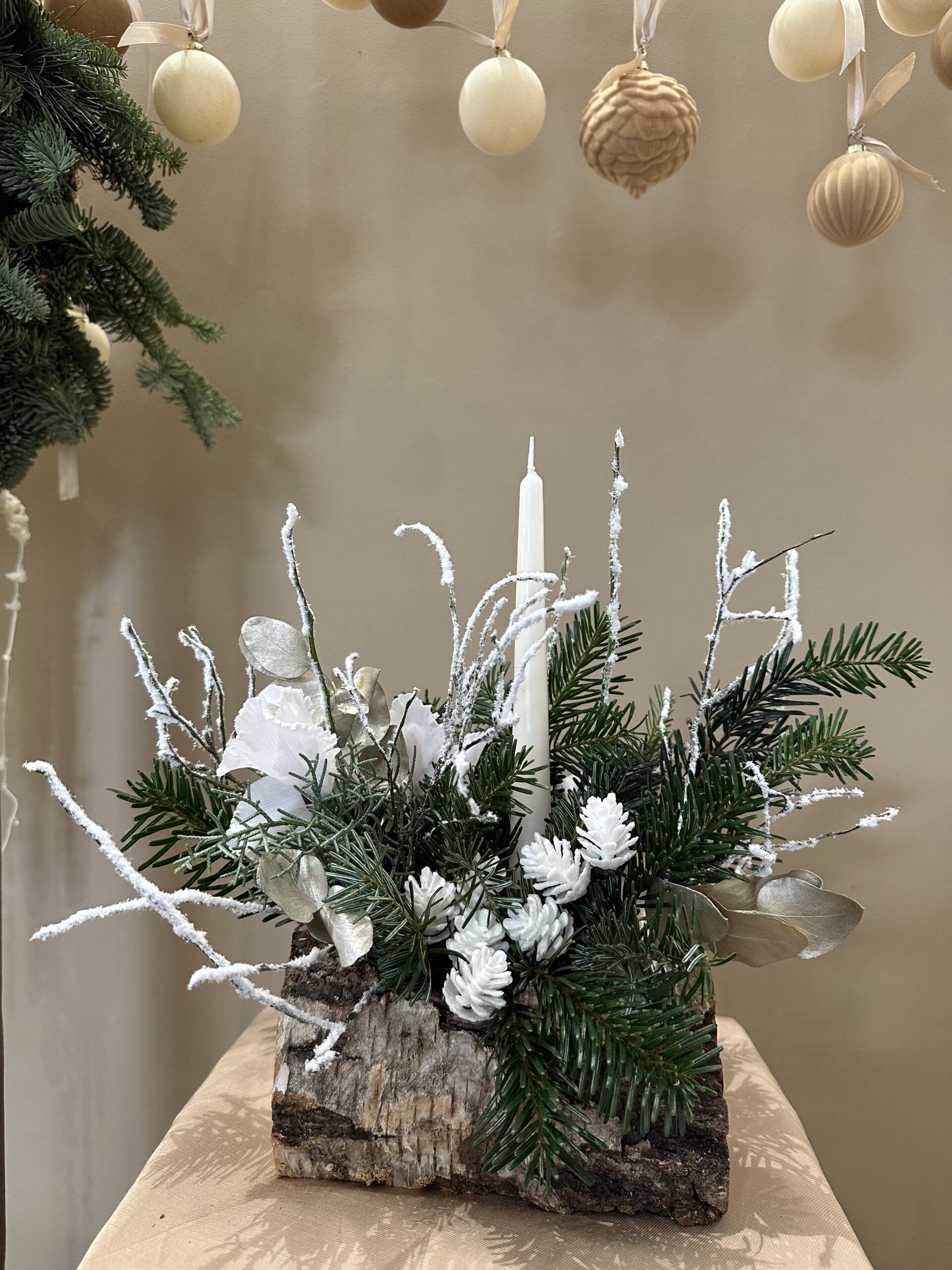 Bûche végétale L’Enneigée, feuillages clairs, mousse poudrée, textures givrées et accessoire monochrome blanc, création Parenthèse Florale Lyon.